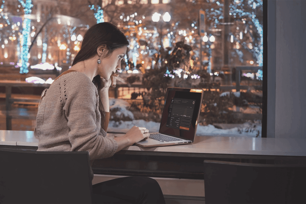 A woman sits at counter using laptop with IPVanish enabled to hide ip address