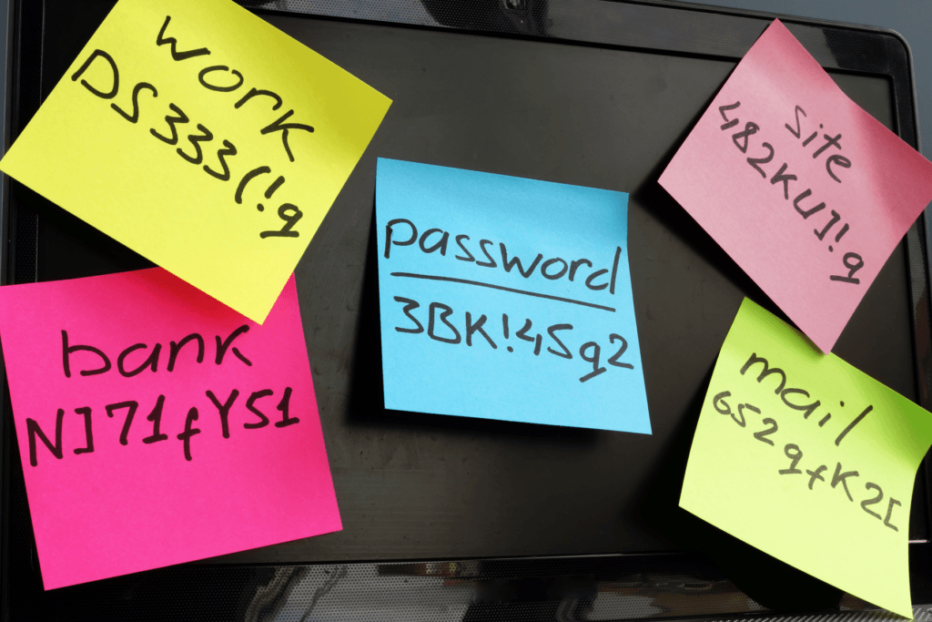 Multi-colored post-it notes with passwords are stuck to a black computer monitor, demonstrating the need for password managers