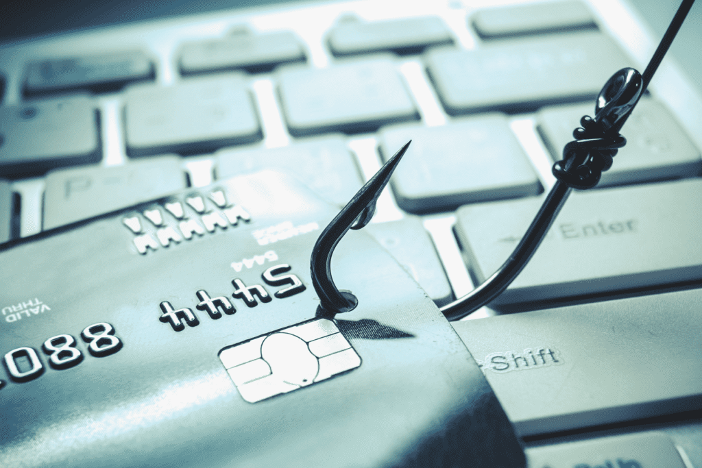 Phishing is visually depicted with a fishing hook with a credit card on the line laying across a computer keyboard