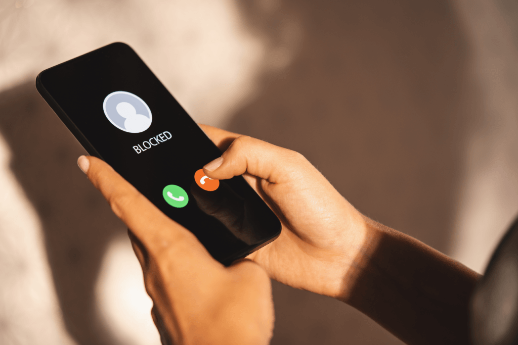 Image shows a person holding a iPhone with a blocked number as they hope to determine what happens when you block a number on iPhone
